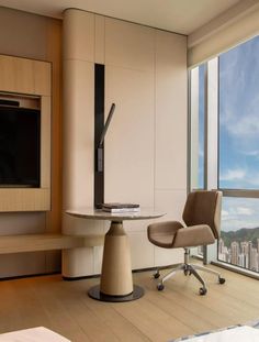 a room with a desk, chair and large window overlooking the cityscape is shown