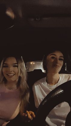 two women sitting in the drivers seat of a car, one is smiling at the camera