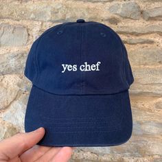 "Introducing our stylish cap featuring the words \"Yes Chef\" embroidered on the front in a minimalist font. Made with high-quality materials, this cap is perfect for those who want to make a statement while keeping it simple. Not only does this cap feature a bold statement, but it also offers the option for customisation. You can add your initials or name on the back of the cap to make it truly unique to you. Cap Styles/Colourways: We have two cap styles that you can choose from: CLASSIC: The classic cotton dad cap has an unstructured, low profile styling, and features an adjustable buckle on the back, ensuring a comfortable and secure fit for all head sizes. Choose from any of our classic colours: Navy, Black, Beige, Pale Blue, Pink, Mint Green, Lemon. CORDUROY: The corduroy cap is made Chef Cap, Yes Chef, Art Merch, Corduroy Cap, Minimalist Font, Cool Gift Ideas, Stylish Caps, Sweatshirts Quotes, Keeping It Simple