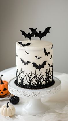 a white cake with black decorations and bats on it, sitting on a table next to pumpkins