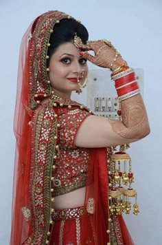 a woman in a red and gold bridal outfit holding her hands up to her face