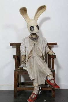 a white rabbit sitting on top of a wooden chair next to a wall and wearing red shoes