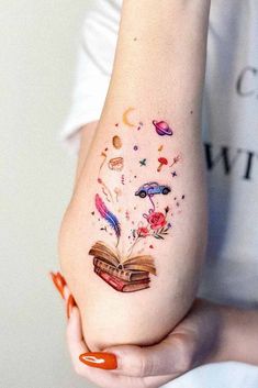 a woman is holding an open book tattoo on her left arm and it's pages flying out