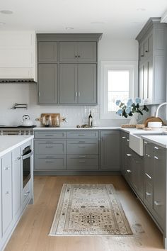 a kitchen with gray cabinets and white counter tops, an area rug on the floor