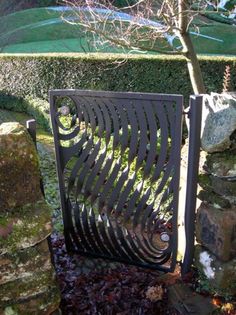 an iron gate in the middle of a stone wall with trees and rocks behind it