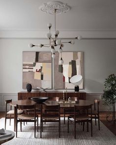 a dining room table and chairs with paintings on the wall behind them in an elegant style