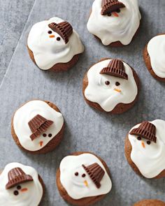 frosted cookies decorated like snowmen with chocolate hats on their heads and noses, sitting on a baking sheet