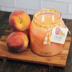 two peaches sitting on top of a wooden cutting board next to a jar of candle