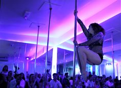 a woman is on the pole in front of a large crowd at an event with purple lighting