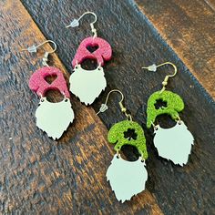 three pairs of earrings with green, pink and white designs on them sitting on a wooden surface