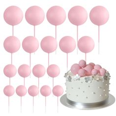 a white cake with pink and silver decorations on it, surrounded by small round balloons