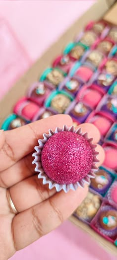 a hand is holding a pink cupcake with sprinkles on it in front of a box