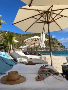 an umbrella and hat on the beach with people in the water behind it, near some lounge chairs