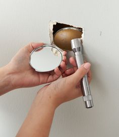 a person is holding a mirror and a hair dryer in their hand while they are peeling the wall