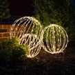 three circular lights are lit up in the garden at night, with trees and bushes behind them