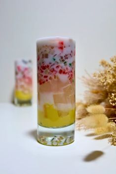 two shot glasses filled with liquid and candy canes on a white surface next to dried flowers