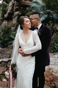 a bride and groom standing next to each other in front of some rocks with plants