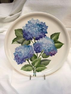 a plate with blue flowers painted on it sitting on a white cloth covered tablecloth