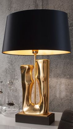 a table lamp with a black shade on it and a gold vase next to it