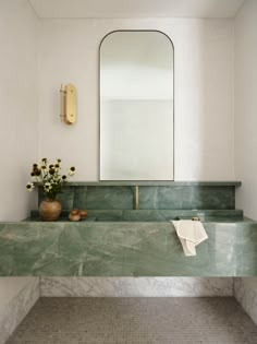 a green marble sink in a bathroom with a mirror above it and flowers on the counter