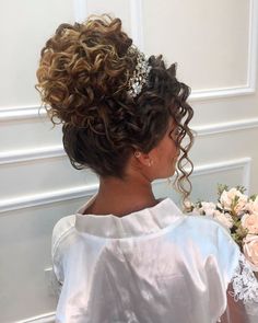 a woman with curly hair wearing a white dress and holding a bouquet of flowers in her hand