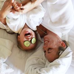 two people laying on a bed with cucumber slices on their faces and eyes