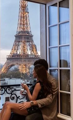 a woman sitting on a window sill looking out at the eiffel tower