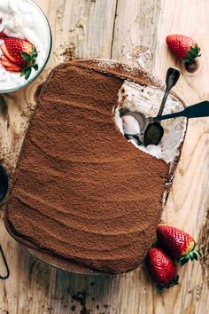 a cake with chocolate frosting and strawberries on the side, next to a bowl of whipped cream