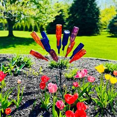 colorful glass flowers are in the middle of a flower bed with grass and trees behind them