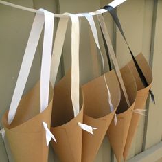 several brown paper bags hanging from a wall with white ribbons attached to them and tied together