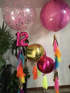 balloons and streamers are hanging from the ceiling in front of a wall with plants