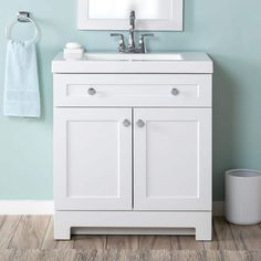 a white bathroom vanity with blue walls and wood flooring in the corner, next to a trash can