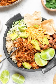 a bowl filled with shredded meat, beans, avocado and tortilla chips