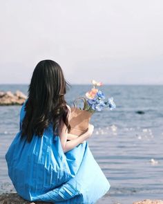 a woman sitting on the beach holding a bouquet of flowers in her lap and looking out at the water