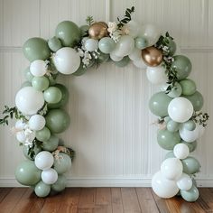 a balloon arch with green, white and gold balloons in the shape of a wreath