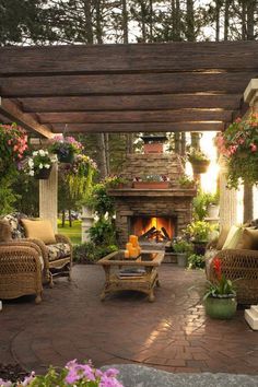 an outdoor living area with wicker furniture and flowers around the fire place, surrounded by greenery