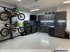 two motorbikes are in the middle of a garage with black cabinets and counters