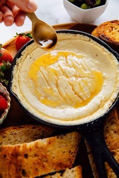 a person spooning some food into a bowl with bread and strawberries in the background