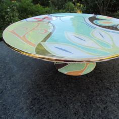 a multicolored glass plate sitting on top of a black stone table in front of some bushes