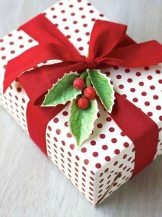 a present wrapped in white and red paper with a holly on the top that says gracias por 12 messe de cario y amistaad