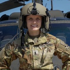 a woman in uniform standing next to a helicopter with her hands on her hips and smiling at the camera