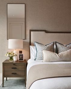 a bedroom with a bed, night stand and mirror on the wall above it's headboard