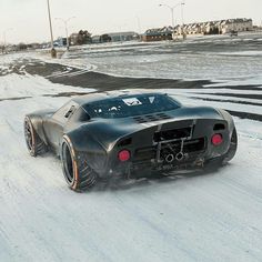 a black sports car driving down a snow covered road in the middle of winter time