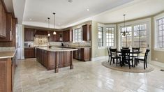 a large open kitchen and dining room with tile flooring, wood cabinets and marble counter tops