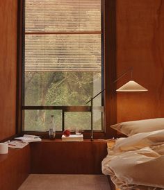 a bed sitting under a window next to a wooden desk with a lamp on it