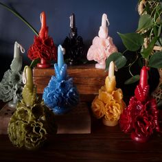 four different colored vases with flowers in them sitting on a wooden table next to a potted plant