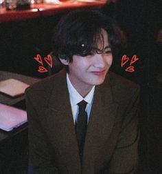 a man in a suit and tie sitting at a table with two hearts drawn on his forehead