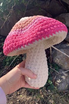 a hand holding up a pink and white crocheted mushroom