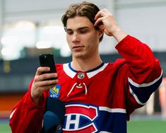 a young man holding a cell phone in his right hand and wearing a red jersey