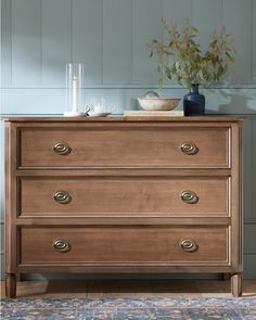 a chest of drawers with two vases on top and one plant in the middle